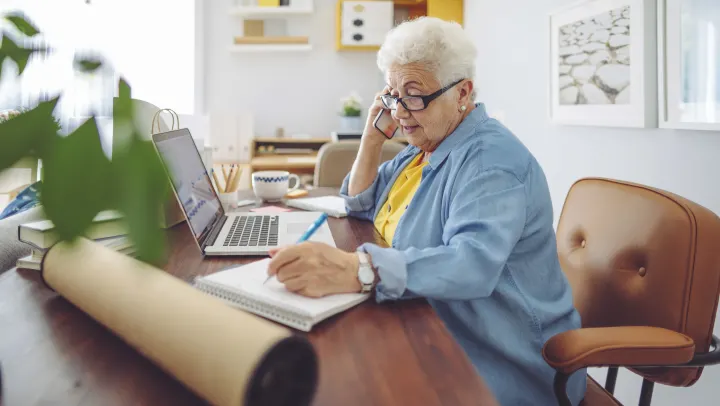 elderly woman on phone with laptop in front of her