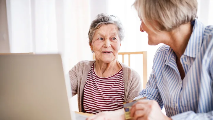 younger woman assisting elderly woman with laptop